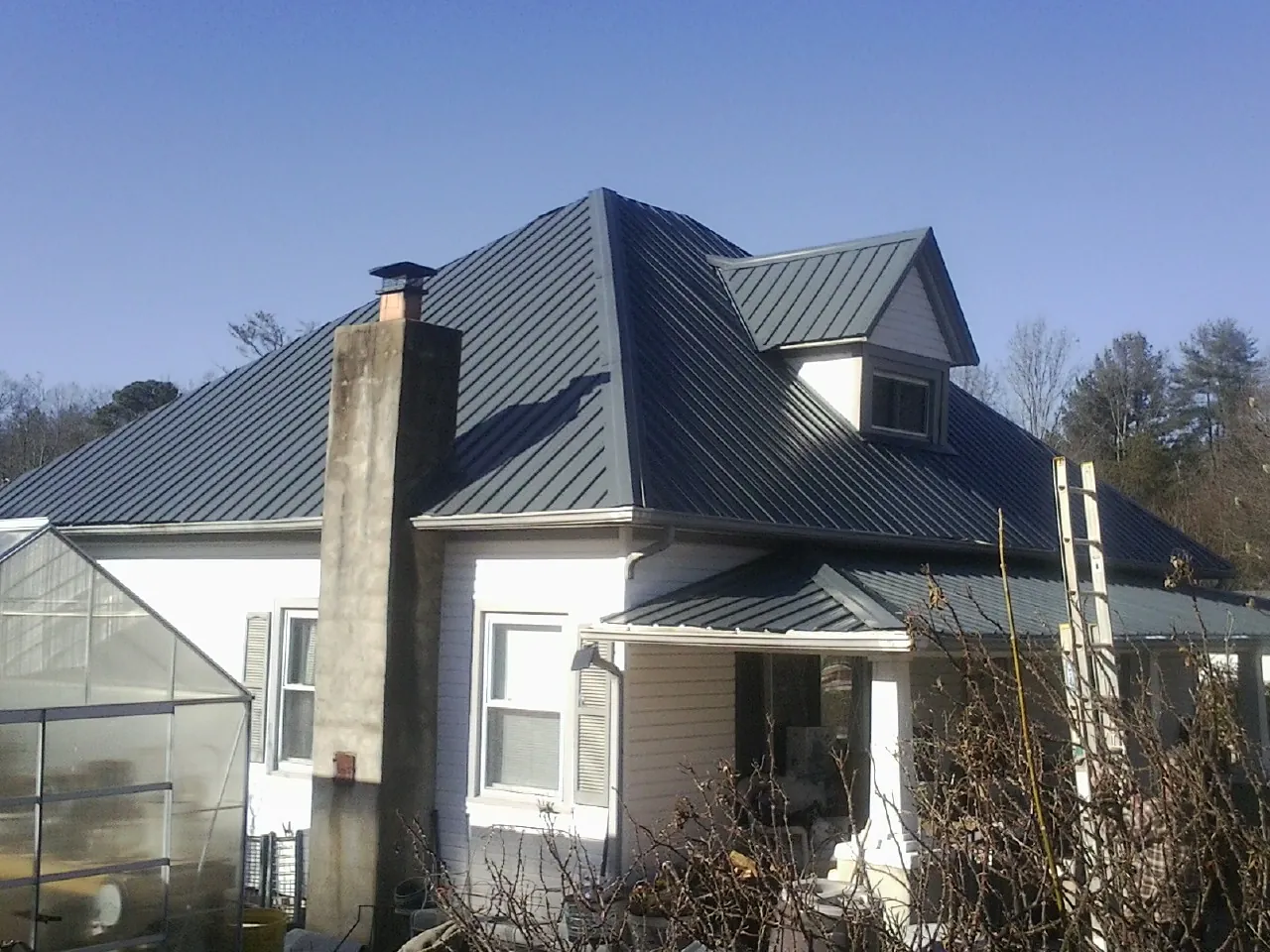 Dark blue standing seam metal roof on a white farmhouse with dormer — Slate & Tile Roof Repair by Roofing Brothers in Needham Heights