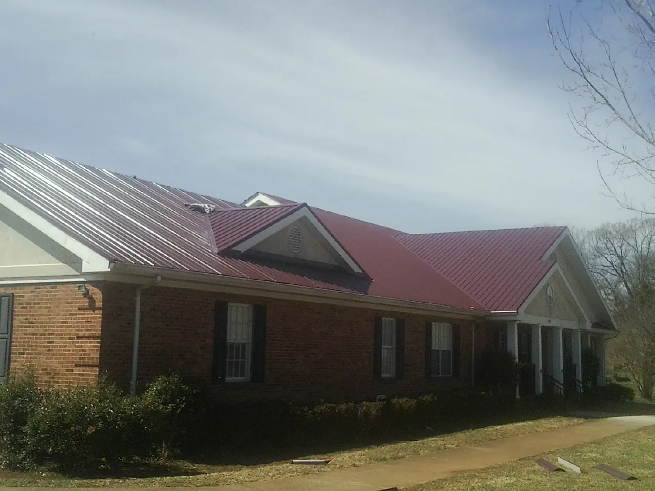 Red metal roof with gabled entries on a long brick building, from a Hail Damage Roof Repair job in Needham Heights