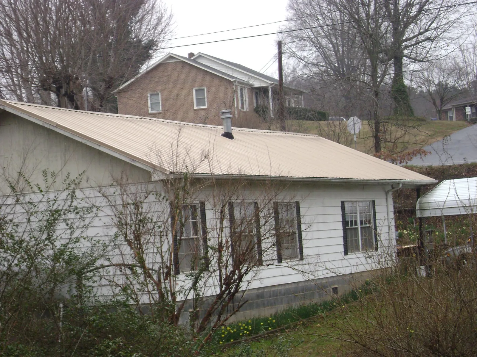 Tan metal roof on a white sided house set into a hillside — Commercial Roofing by Roofing Brothers in Needham Heights