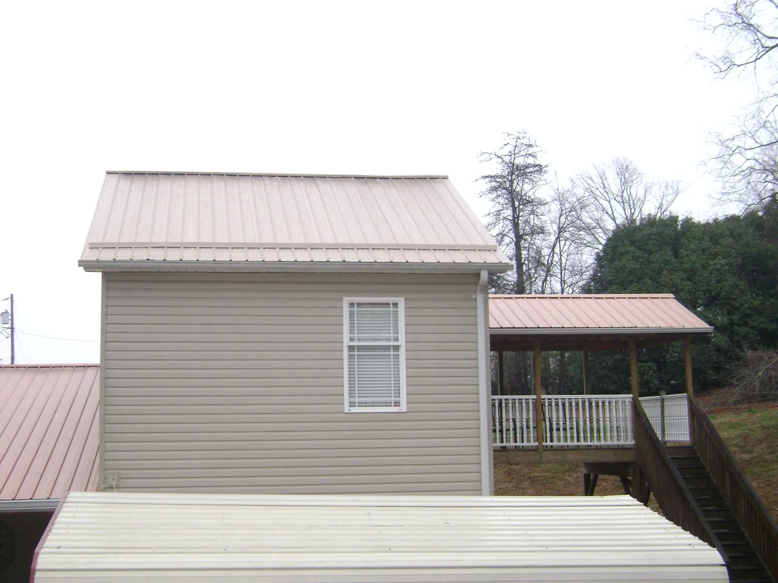 Tan metal roofs on a two story addition and attached porch, from a Roof Replacement job in Needham Heights