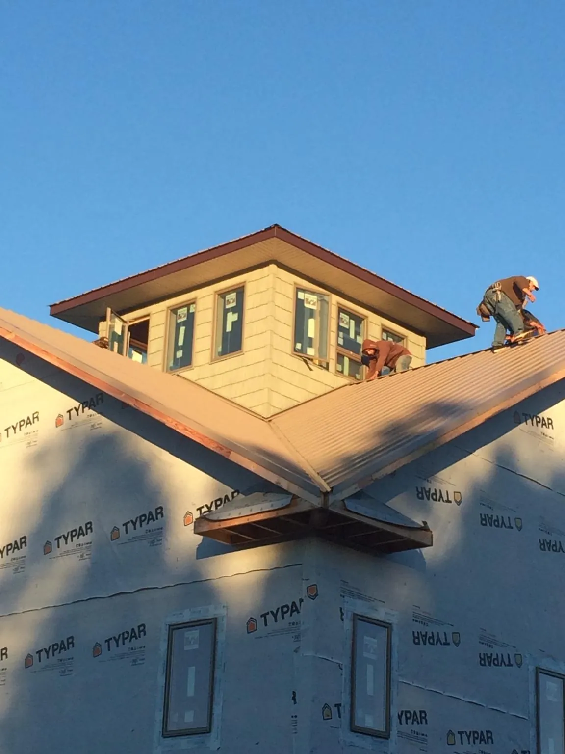 Roofers working around a rooftop cupola on a new metal roof at sunset — Roof Waterproofing in Needham Heights by Roofing Brothers